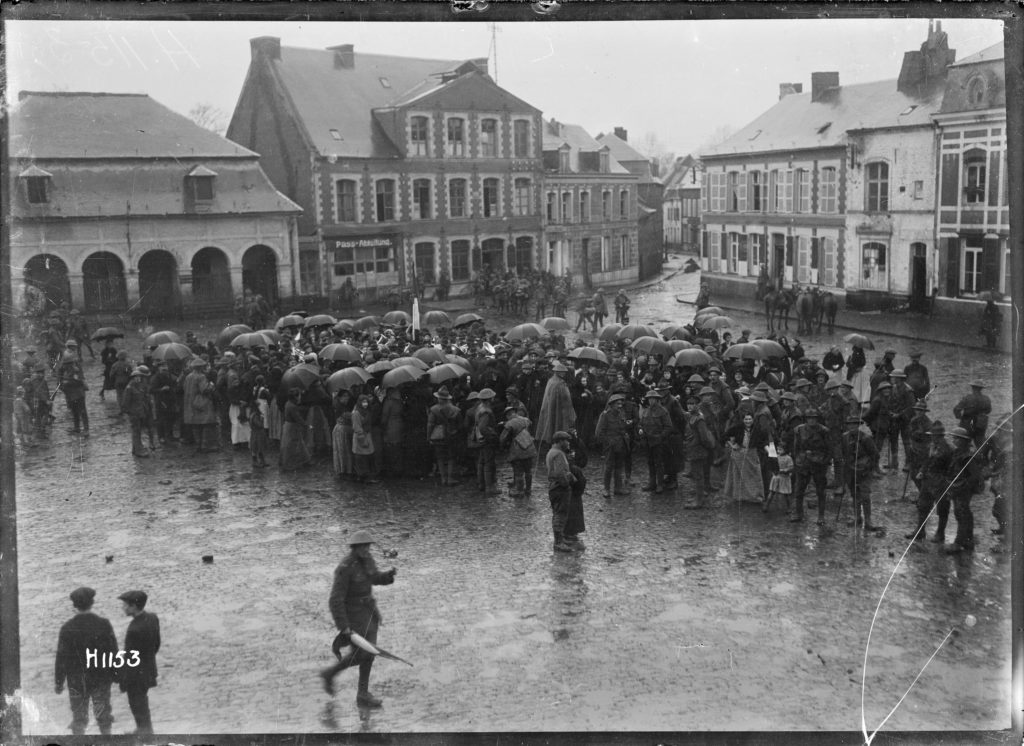 A crowd stand around a New Zealand regimental band playing in Le Quesnoy, the day after its capture. 5th Nov 1918.Photographed by Captain H. A Sanders. H1153. NZ RSA Collection. Alexander Turnbull Library, Wellington, New Zealand.